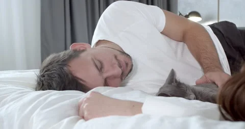 A man is lying on the bed with his girlfriend and a cat and petting it, 4k Stock Footage 135376329