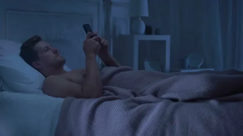 Man lying in bed holding phone, turning away from woman coming in lingerie Stock Footage 98143057