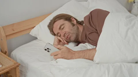 Man lying in bed holding smartphone with hand, smiling while scrolling the .. Stock Footage 337375844