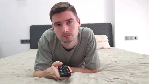 Man lying on bed holding a TV remote control. Indoor portrait in a bedroom Video stock 284044550
