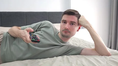 Man lying on bed holding TV remote control and switching channels Stock Footage 284044577