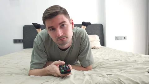 Man lying on a bed holding a TV remote control and switching channels Stock Footage 284044603