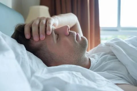 Man lying in bed at home suffering from headache or hangover Stock Photos