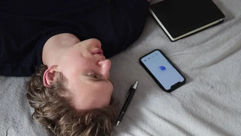 Man lying on bed looks at smartphone screen with calm expression communication w Stock Footage 314979796