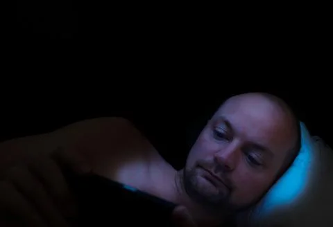 Man lying in bed at night looking at his tablet. Stock Photos