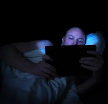 Man lying in bed at night looking at his tablet. Stock Photos