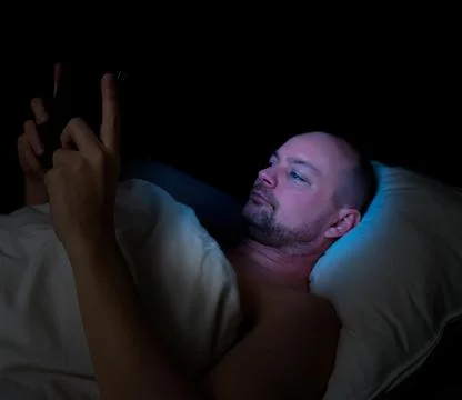 Man lying in bed at night looking at his tablet. Stock Photos