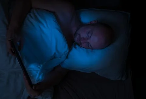 Man lying in bed at night looking at his tablet. Stock Photos