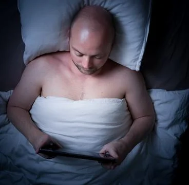 Man lying in bed at night looking at his tablet. Stock Photos