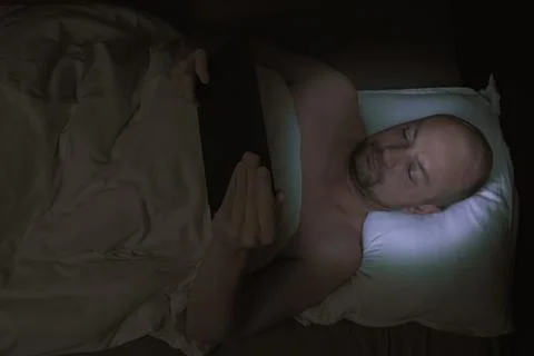 Man lying in bed at night looking at his tablet. 스톡 사진