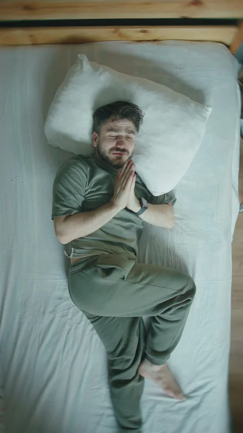 Man lying in bed praying with folded hands before falling asleep, top view .. Stock Footage 344469492