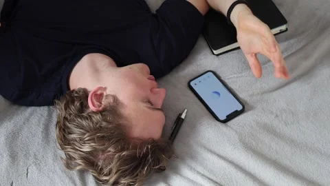Man lying on bed raises hand while talking to smartphone feeling open and relaxe Stock Footage 314979768