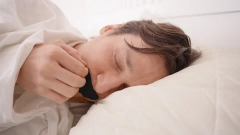 Man Lying in Bed Removing Mouth Tape with Eyes Closed and Pained Expression Then Stockbeeldmateriaal 306034602