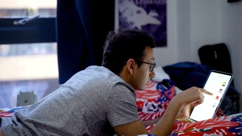 Man lying in bed scrolling iPad Pro in bedroom, browsing, iPad, entertainment Stock Footage 129153644