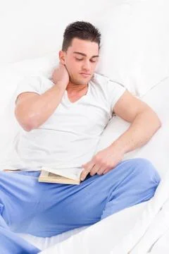 Man lying in bed suffering from neck pain reading book Stock Photos