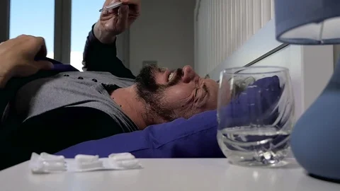 Man lying in bed taking thermometer slow motion Stock Footage 77423211