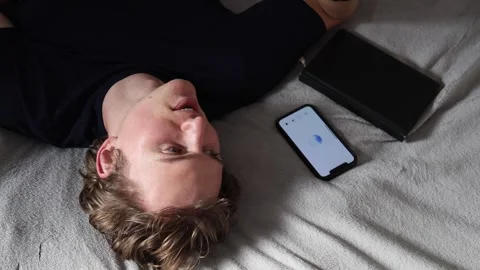 Man lying on bed talks to artificial intelligence on smartphone with notebook ne Stock Footage 314979679