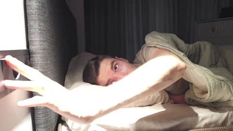 Man lying in bed under a blanket reaching to turn off the bedside light Stock Footage 284042355