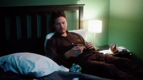 Man lying in bed using smartphone and eating chips at night Vídeos de archivo 319442693
