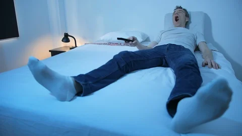 A man is lying in a bed watching tv, operating a remote control Stock-Footage 128325266