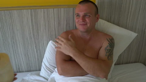 A man is lying in bed. A woman's hand gives a woman a young coconut with a straw Stock Footage 91705997