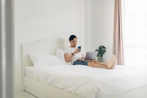 Man lying on bed work on his laptop in cozy white bedroom. Foto stock