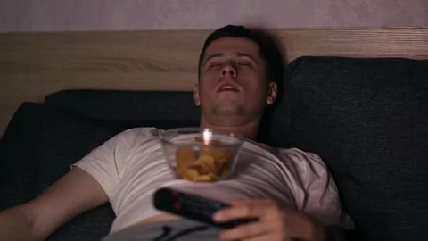 A man lying at coach and watching TV, eating fastfood Stock Footage 150169345