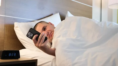 A man lying comfortably in bed is checking his phone while in a hotel room Vídeo Stock 306112016
