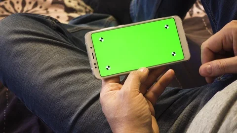 The man is lying on the couch and is holding a phone with a green screen. You Video stock 88540151