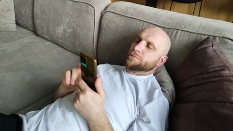 Man lying on couch and looking at smartphone screen. Handsome bearded guy Stock Footage 311152205