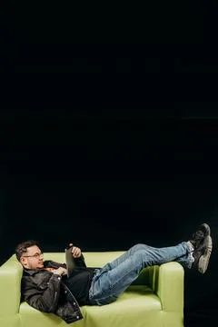 A man is lying on the couch and playing a tablet on a black background Stock Photos