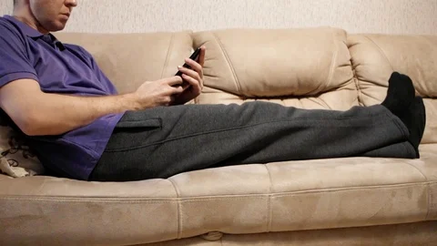 A man is lying on the couch and uses a smartphone-is in social network Stock Footage 122508453