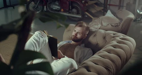 A man lying on the couch with the book in his arms reads. Stock Footage 144529411