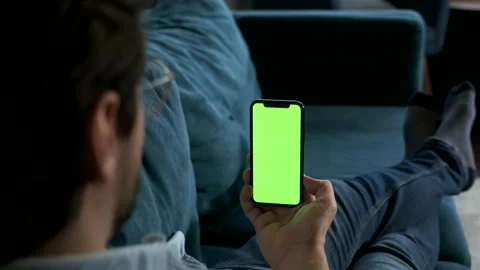 Man lying on couch at night, holding a smartphone with chroma key mock up Stock Footage 144683179