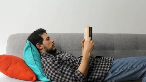 A man lying on a couch reading a text book in a peaceful attitude Video stock 340583351