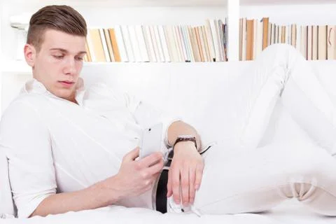 Man lying on the couch texting message on cellphone Stock Photos