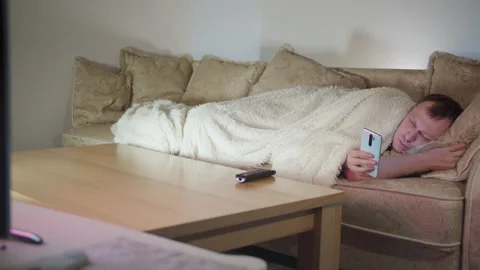 A man lying on the couch by the TV at night, using his cell phone, copy space Stock Footage 161132653