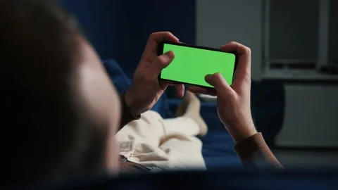 Man lying on couch using smart phone with chroma key green screen at night Stock Footage 144311459