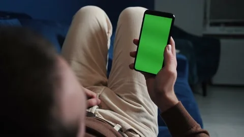 Man lying on couch using smart phone with chroma key green screen at night Stock Footage 144311489