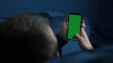 Man lying on couch using smart phone with chroma key green screen at night Stock Footage 144490076