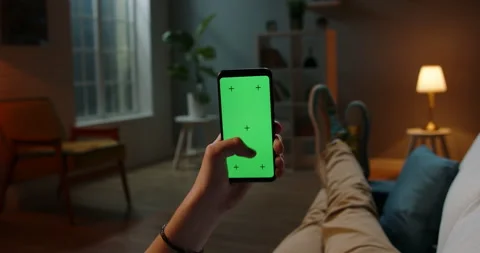 Man lying on couch using smartphone with chroma key green screen at night Stock Footage 132068649