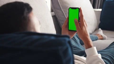 Man lying on couch using smartphone with chroma key green screen , scrolling 스톡 동영상 138904798