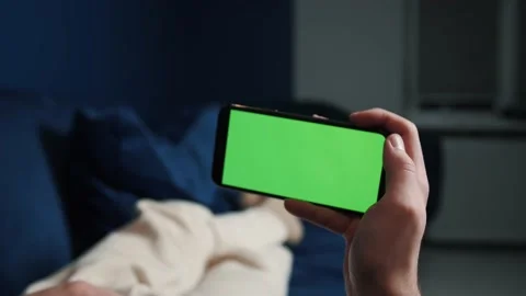 Man lying on couch using smartphone with chroma key green screen at night Video stock 144311210