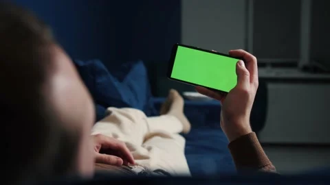 Man lying on couch using smartphone with chroma key green screen at night Stock Footage 144311325