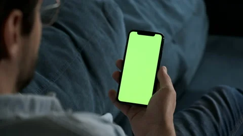 Man lying on couch using smartphone with chroma key green screen at night Stock Footage 144682721