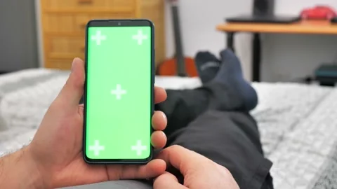 Man lying on couch using smartphone with chroma key green screen at night Stock Footage 224142197