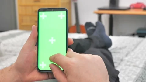 Man lying on couch using smartphone with chroma key green screen at night Stock Footage 224530817
