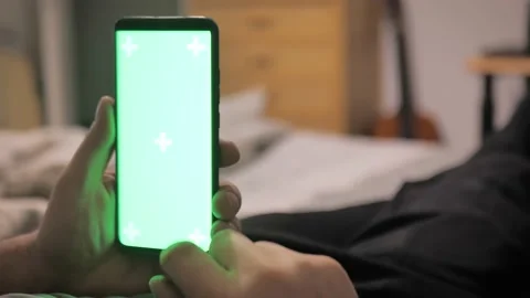 Man lying on couch using smartphone with chroma key green screen at night Stock Footage 226627159