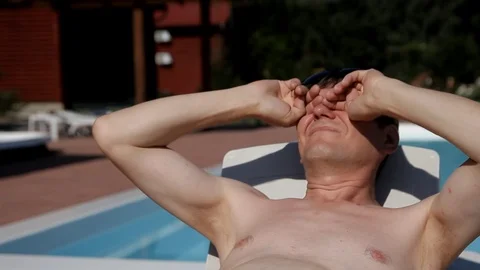 A man lying on a deck chair rubs his eyes and puts on dark glasses Stock Footage 99935059