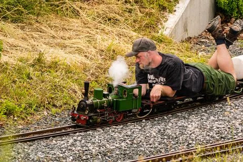 A man lying down drives a model of a steam locomotive Stock Photos